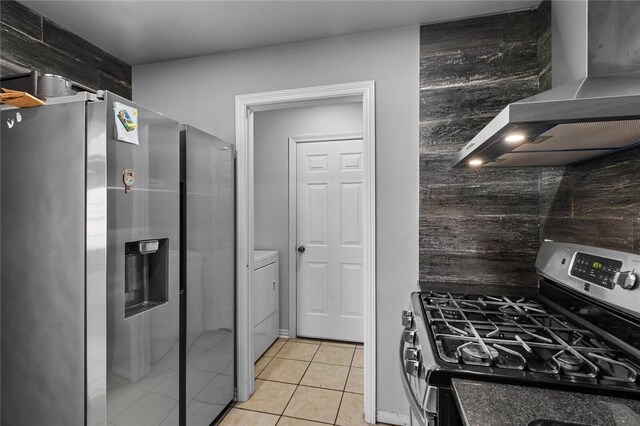 kitchen featuring wall chimney range hood, washing machine and dryer, light tile patterned flooring, and appliances with stainless steel finishes