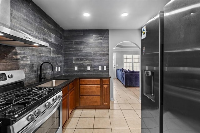 kitchen with tasteful backsplash, light tile patterned floors, arched walkways, brown cabinetry, and stainless steel appliances