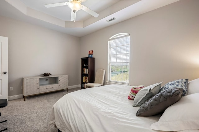 carpeted bedroom with a raised ceiling, baseboards, and a ceiling fan
