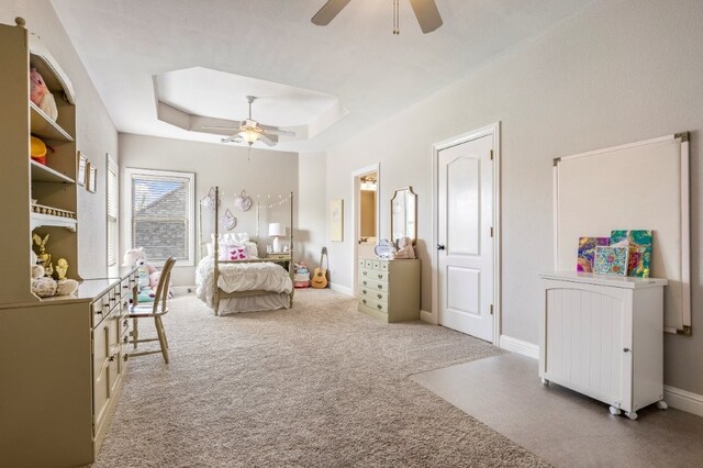 carpeted bedroom with a tray ceiling, a ceiling fan, and baseboards