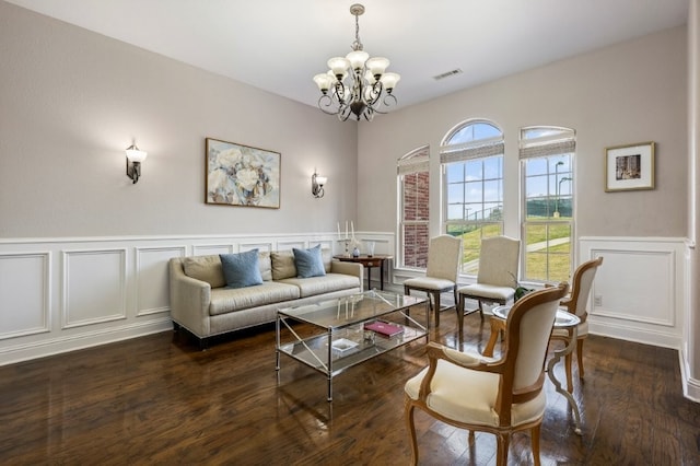 living area featuring a decorative wall, a chandelier, dark wood-style floors, and wainscoting