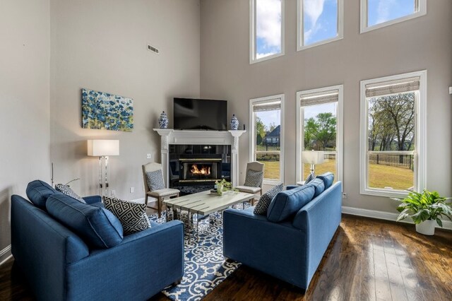 living area featuring a high ceiling, a glass covered fireplace, dark wood finished floors, and baseboards