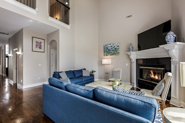 living area featuring arched walkways, a high ceiling, wood finished floors, a tile fireplace, and baseboards