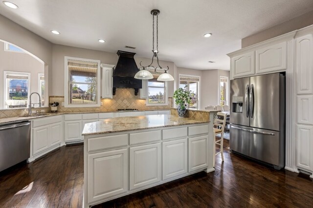 kitchen with appliances with stainless steel finishes, custom range hood, a sink, decorative backsplash, and white cabinets
