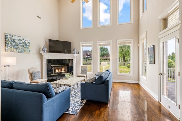 living area featuring a fireplace, dark wood finished floors, a high ceiling, a ceiling fan, and baseboards