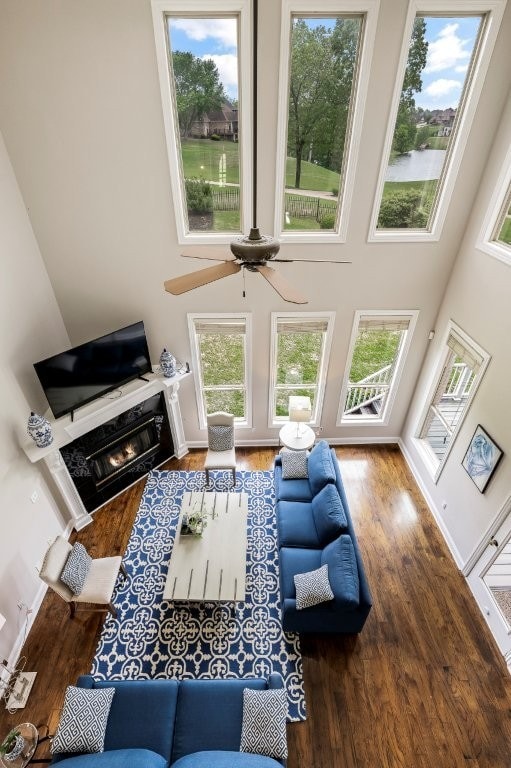living room with wood finished floors, plenty of natural light, a ceiling fan, a towering ceiling, and a premium fireplace