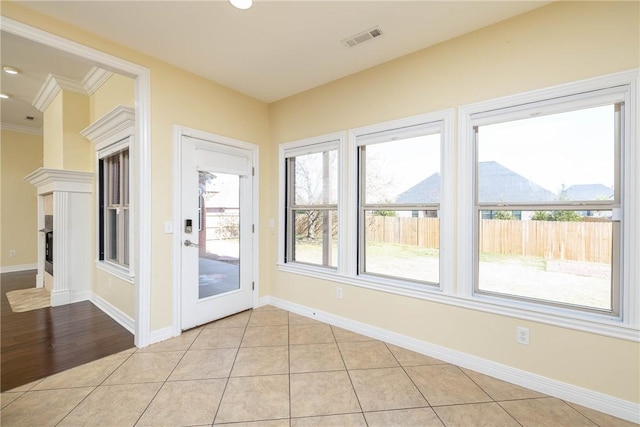 doorway with visible vents, baseboards, crown molding, a fireplace with flush hearth, and light tile patterned flooring