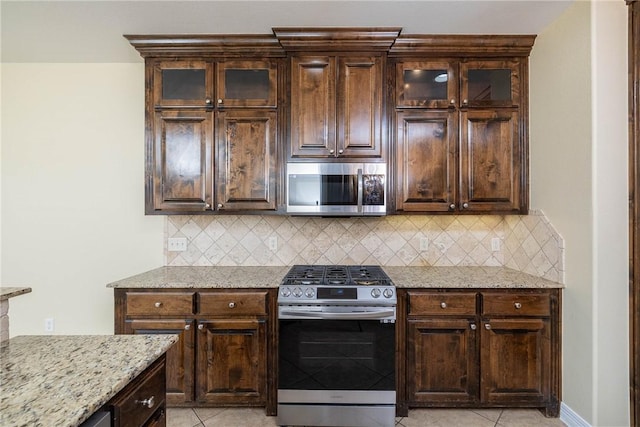 kitchen with dark brown cabinetry, light tile patterned floors, backsplash, and stainless steel appliances