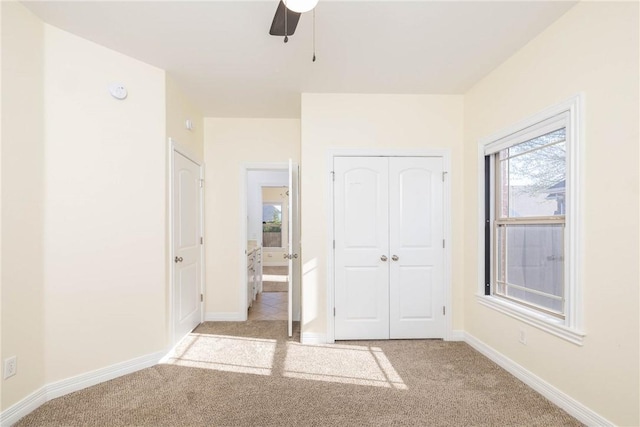 unfurnished bedroom with a closet, baseboards, a ceiling fan, and light colored carpet