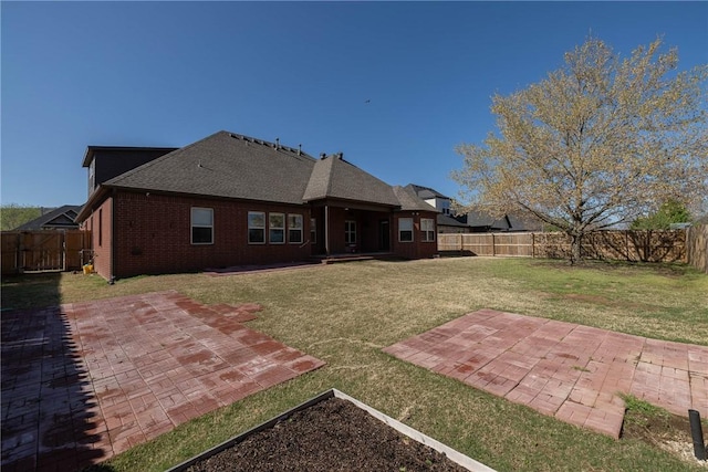 back of property with a shingled roof, a patio area, a lawn, a fenced backyard, and brick siding