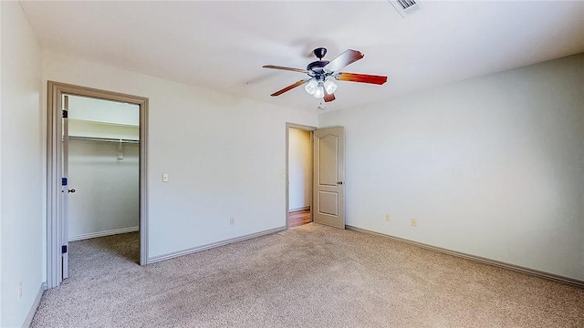 unfurnished bedroom featuring ceiling fan, light colored carpet, a spacious closet, visible vents, and baseboards
