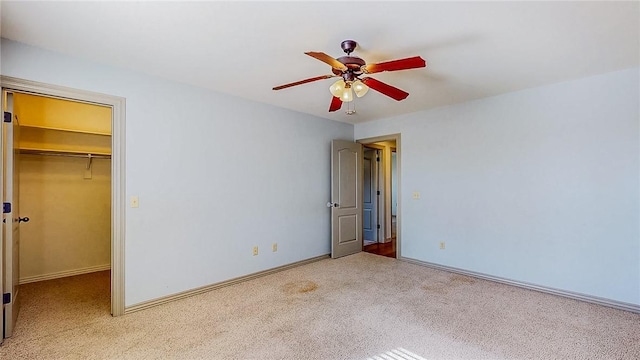 unfurnished bedroom featuring ceiling fan, a closet, carpet flooring, a walk in closet, and baseboards