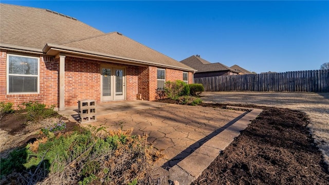 back of property with a patio, fence, roof with shingles, and brick siding