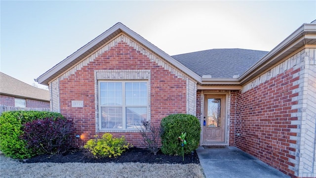 doorway to property featuring brick siding and roof with shingles