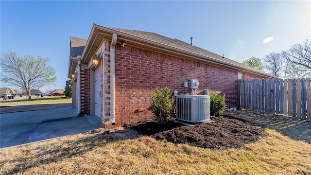 view of home's exterior featuring roof with shingles, brick siding, central air condition unit, and fence