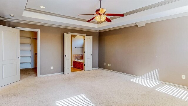 unfurnished bedroom with ornamental molding, light colored carpet, a walk in closet, and a raised ceiling