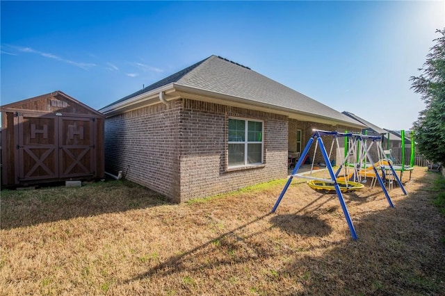 exterior space featuring roof with shingles, an outdoor structure, a shed, brick siding, and a playground