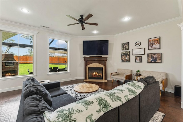 living room with crown molding, visible vents, a ceiling fan, and a glass covered fireplace