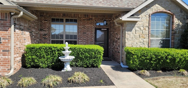 view of exterior entry featuring a shingled roof, stone siding, and brick siding