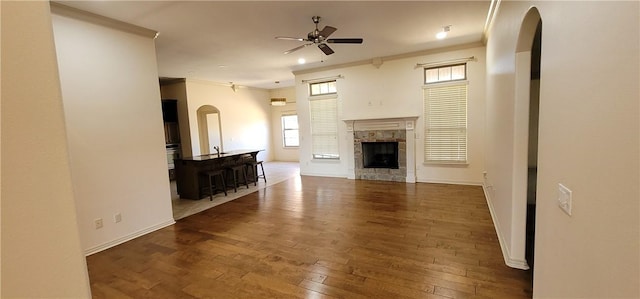 unfurnished living room featuring crown molding, arched walkways, a ceiling fan, wood-type flooring, and baseboards
