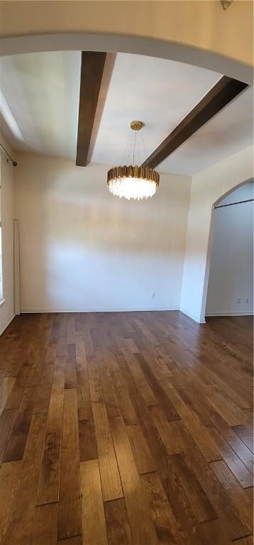 empty room featuring dark wood-type flooring, an inviting chandelier, and beam ceiling