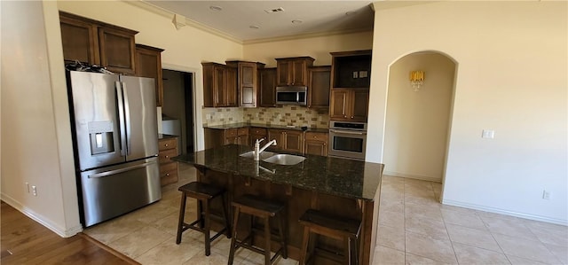 kitchen featuring arched walkways, visible vents, appliances with stainless steel finishes, a sink, and a center island with sink