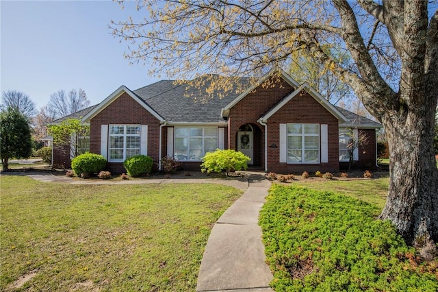 view of front of house featuring brick siding, a front yard, and a shingled roof