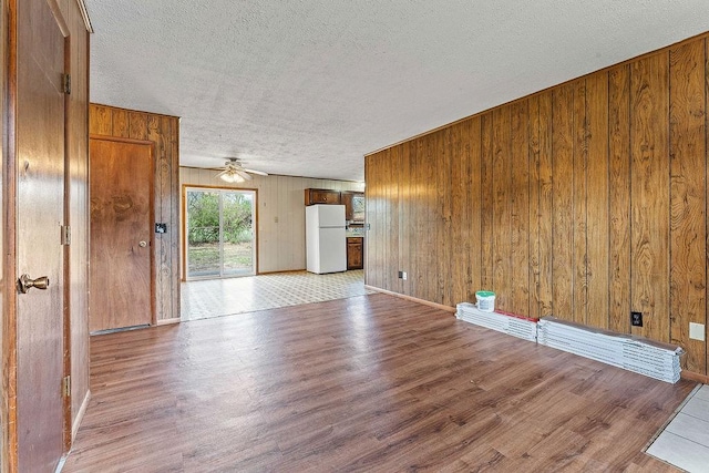 unfurnished living room featuring wooden walls, a ceiling fan, wood finished floors, and a textured ceiling