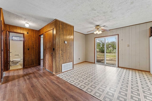 empty room with visible vents, ceiling fan, wood walls, and a textured ceiling
