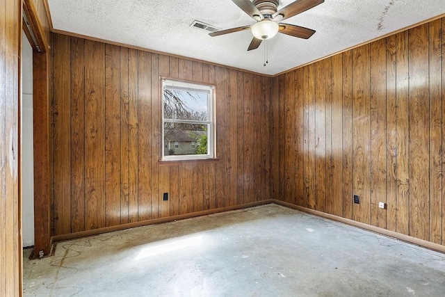 spare room featuring a ceiling fan, visible vents, unfinished concrete floors, wood walls, and baseboards