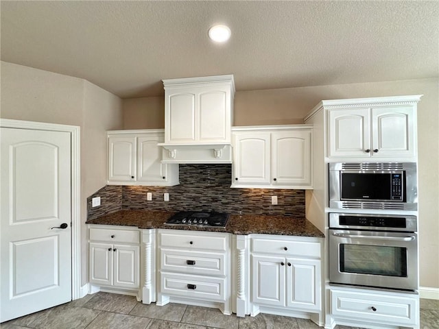 kitchen with backsplash, appliances with stainless steel finishes, white cabinetry, and dark stone countertops