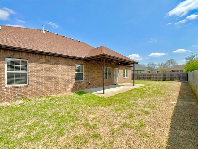 rear view of property with a fenced backyard, a yard, roof with shingles, a patio, and brick siding