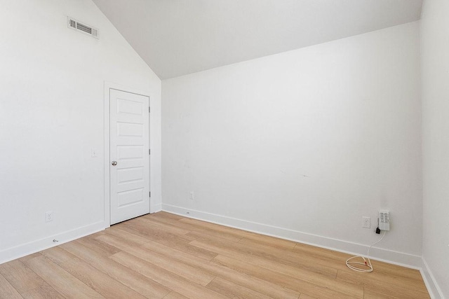 empty room with visible vents, light wood-style flooring, lofted ceiling, and baseboards
