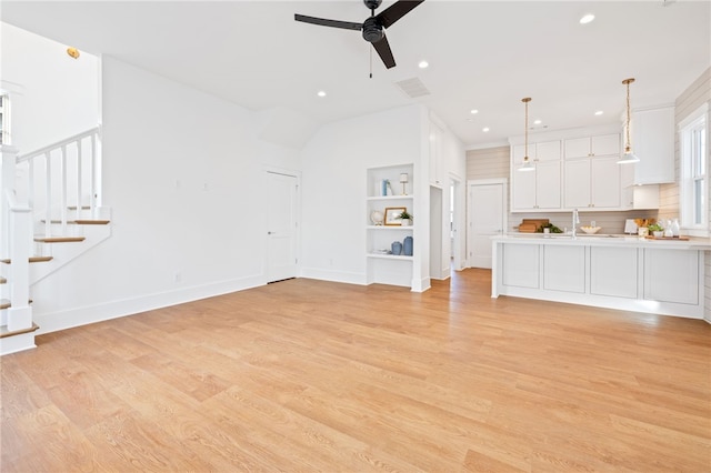 unfurnished living room featuring built in features, baseboards, a ceiling fan, light wood-style floors, and stairs
