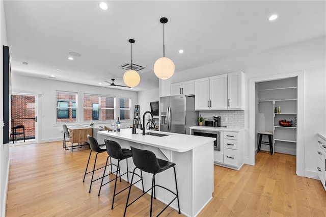 kitchen with a kitchen breakfast bar, stainless steel fridge, light countertops, white cabinets, and a center island with sink