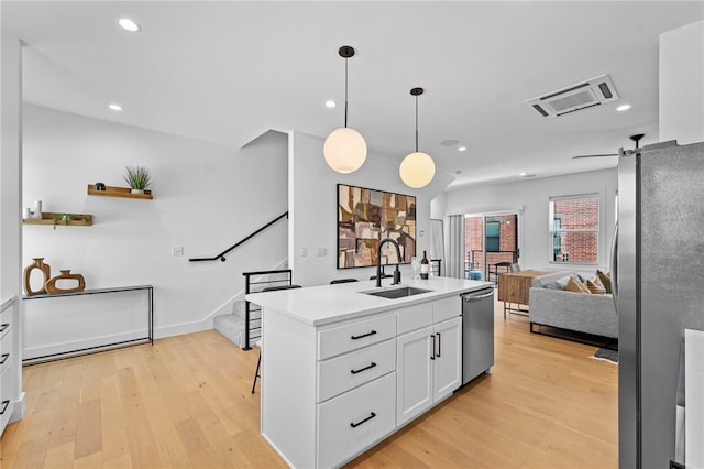 kitchen with white cabinets, a sink, open floor plan, light wood-style floors, and stainless steel appliances
