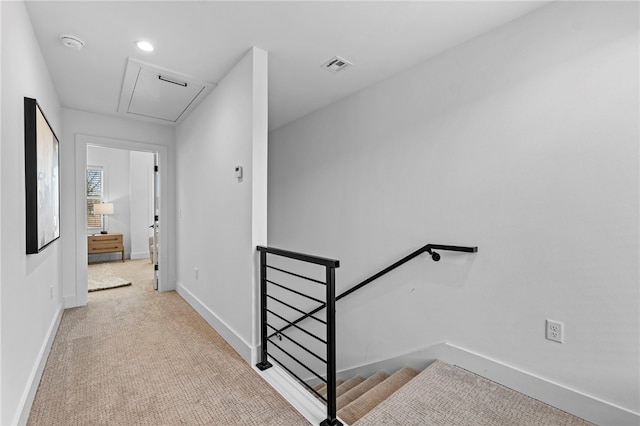 corridor with an upstairs landing, baseboards, attic access, and carpet