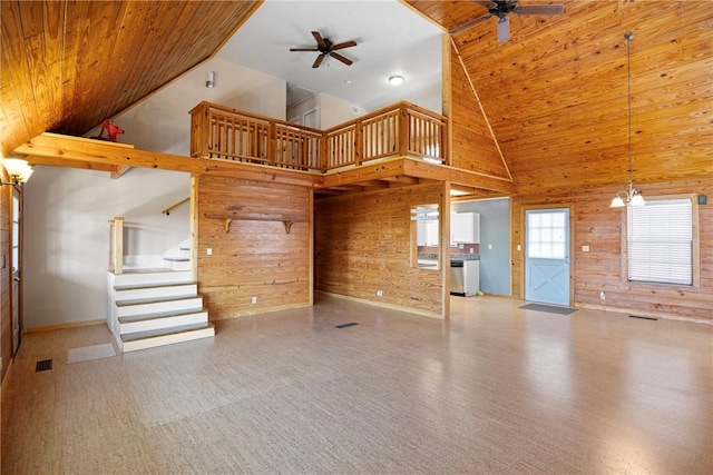 unfurnished living room featuring high vaulted ceiling, wooden walls, ceiling fan with notable chandelier, and wooden ceiling