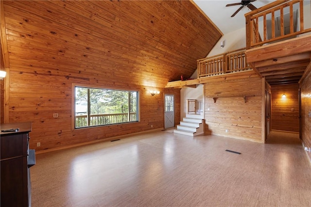 unfurnished living room featuring wood walls, stairs, ceiling fan, high vaulted ceiling, and wood finished floors