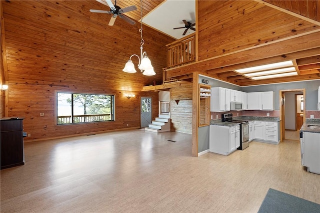 kitchen with wooden walls, a towering ceiling, ceiling fan with notable chandelier, and appliances with stainless steel finishes