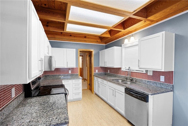 kitchen featuring white cabinets, dark stone countertops, appliances with stainless steel finishes, a sink, and backsplash