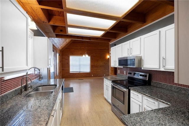kitchen featuring tasteful backsplash, wood walls, white cabinets, appliances with stainless steel finishes, and a sink