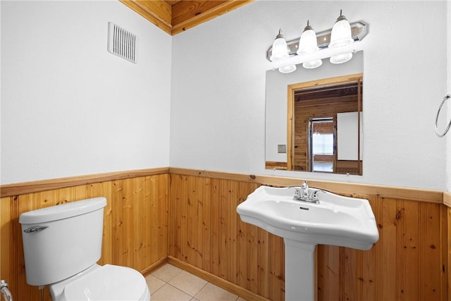 half bath with tile patterned floors, toilet, a wainscoted wall, wood walls, and visible vents