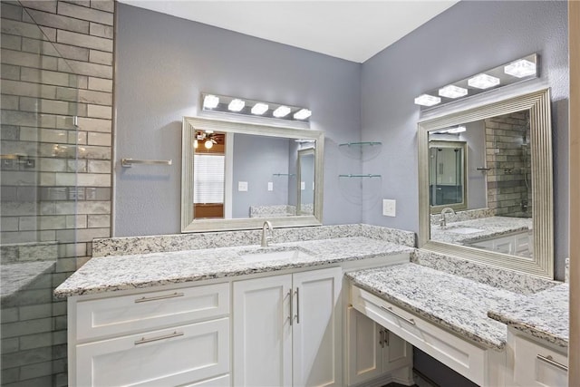 full bathroom with a sink, two vanities, a ceiling fan, and tiled shower