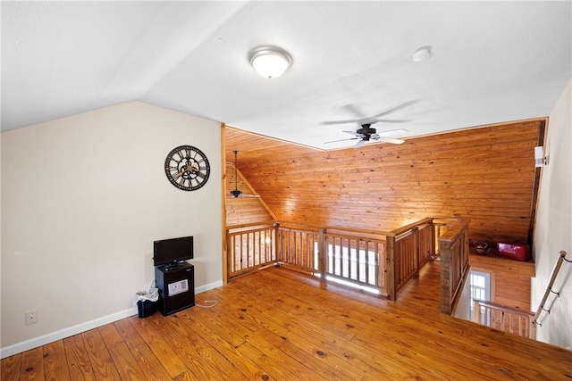 additional living space with baseboards, wooden walls, light wood-style flooring, a ceiling fan, and lofted ceiling
