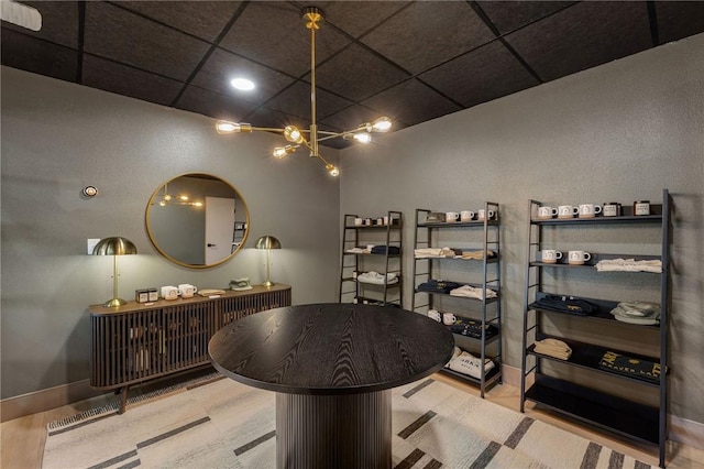 wine area featuring wood finished floors, baseboards, an inviting chandelier, and a drop ceiling