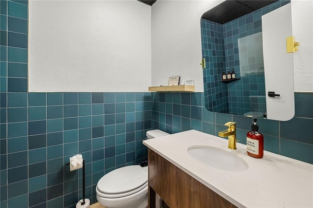 half bath with toilet, tile walls, a textured wall, wainscoting, and vanity