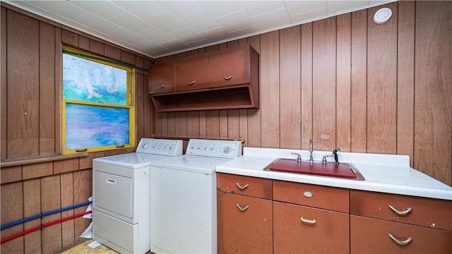 clothes washing area with washing machine and dryer, wood walls, cabinet space, and a sink