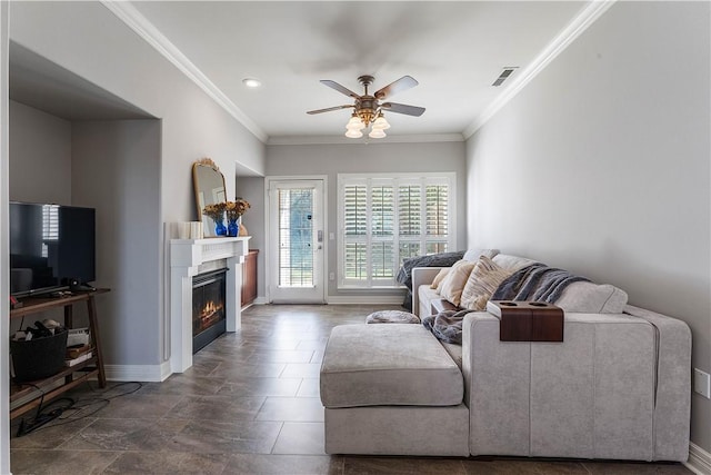 living room with a glass covered fireplace, baseboards, crown molding, visible vents, and ceiling fan
