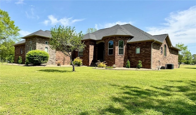 french provincial home featuring brick siding, a front lawn, and central air condition unit